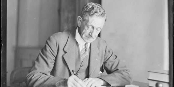 Black and white image of Sir Robert Garran sitting at a desk writing
